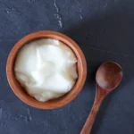Close de uma tigela branca com iogurte grego muito cremoso e denso, com textura firme.