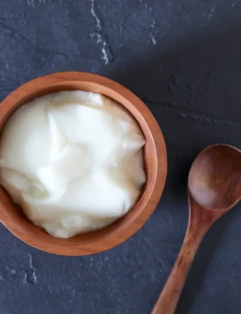 Close de uma tigela branca com iogurte grego muito cremoso e denso, com textura firme.