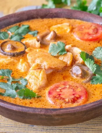 Close de uma tigela de curry vermelho decorada com folhas de coentro verde e rodelas de pimenta vermelha.