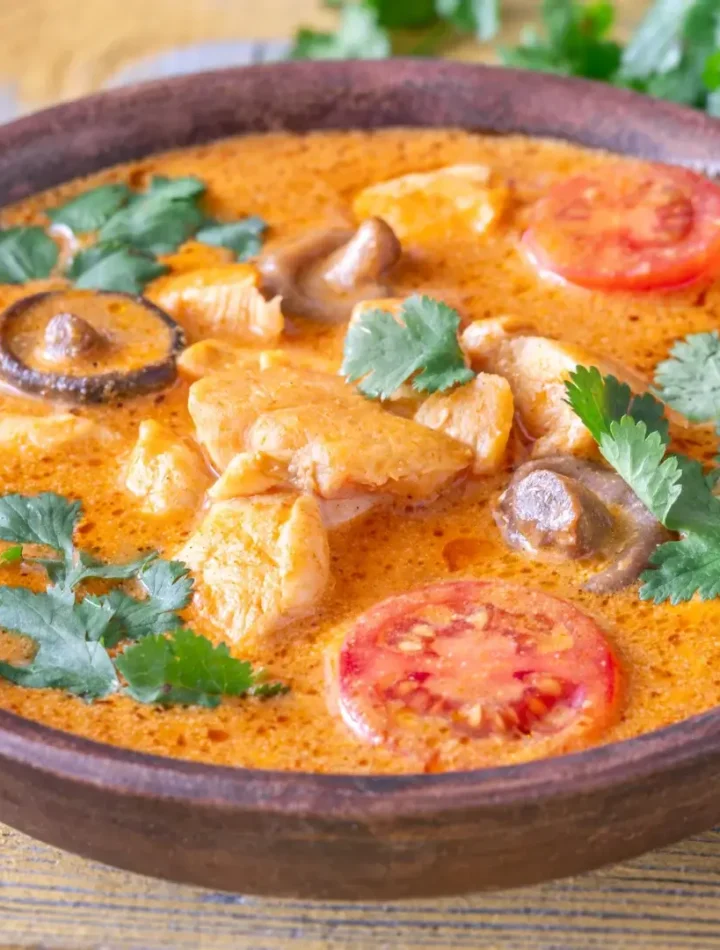 Close de uma tigela de curry vermelho decorada com folhas de coentro verde e rodelas de pimenta vermelha.