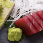 Fatias de sashimi de salmão e atum dispostas em círculo com uma flor de gengibre e pasta de wasabi