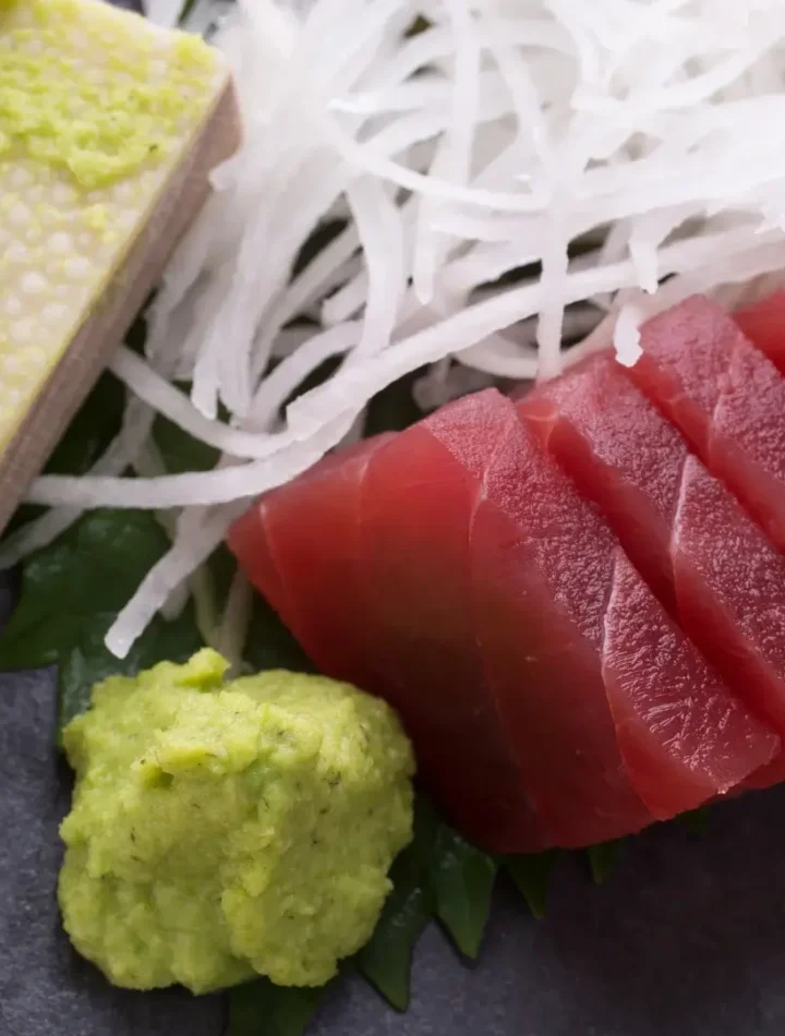 Fatias de sashimi de salmão e atum dispostas em círculo com uma flor de gengibre e pasta de wasabi