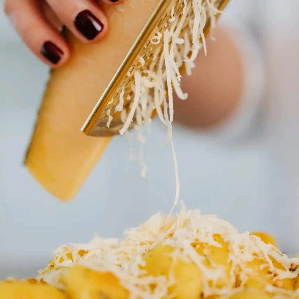 Mãos adicionando uma generosa fatia de manteiga e queijo ralado sobre o arroz quente em uma panela de ferro.