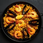 Panela de paella recheada com arroz amarelo, camarões grandes, mexilhões na concha e rodelas de limão.