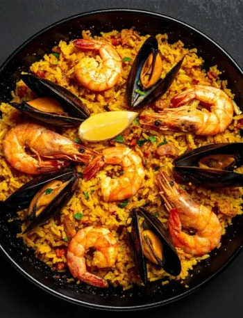Panela de paella recheada com arroz amarelo, camarões grandes, mexilhões na concha e rodelas de limão.