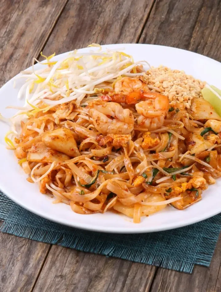 Prato de Pad Thai com camarões grandes por cima, amendoim triturado ao lado e fatias de limão