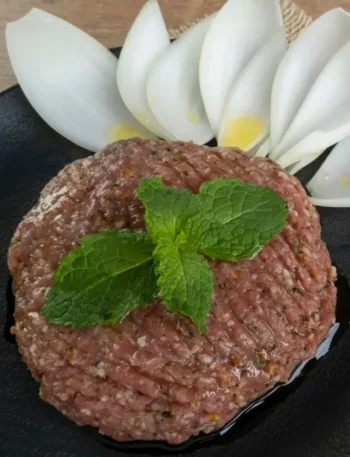 Prato de kibe cru decorado artisticamente com folhas de hortelã verde e muito azeite de oliva por cima.