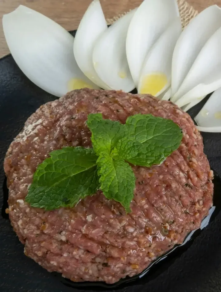 Prato de kibe cru decorado artisticamente com folhas de hortelã verde e muito azeite de oliva por cima.