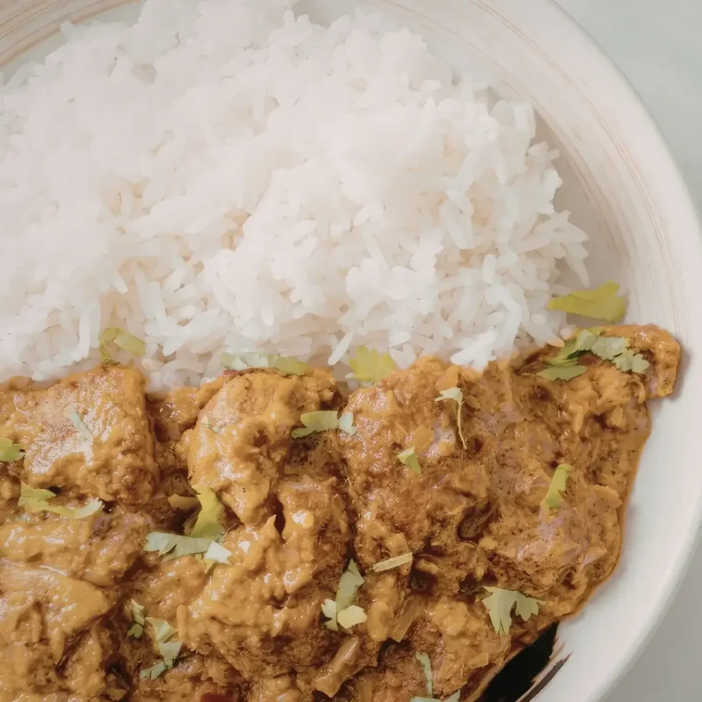 Prato fundo com curry de frango alaranjado e cremoso ao lado de uma porção de arroz branco soltinho.