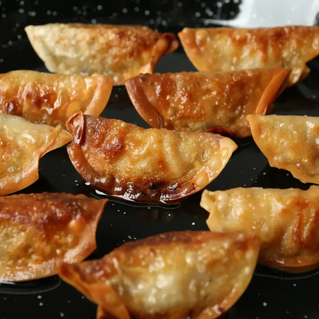 Visão aproximada de gyozas dentro de uma frigideira preta, mostrando a parte inferior bem dourada e crocante.