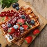 Waffle belga coberto com morangos frescos, mirtilos e polvilhado com açúcar fino.